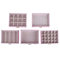 Vue aérienne présentant les tiroirs (vides et posés sur une table) de la grande boîte à bijoux en cuir rose à portes